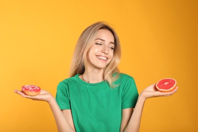 Woman choosing between doughnut and healthy grapefruit on yellow background
