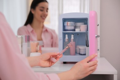 Woman taking face roller out of cosmetic refrigerator indoors, closeup