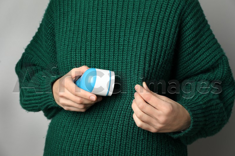 Photo of Woman in woolen sweater using fabric shaver on light grey background, closeup