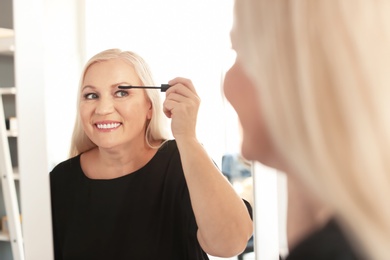 Mature woman applying makeup near mirror at home
