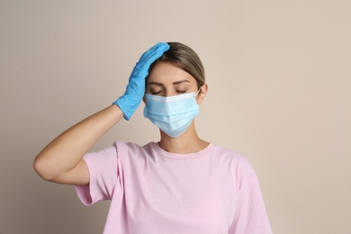 Stressed woman in protective mask on beige background. Mental health problems during COVID-19 pandemic