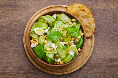 Photo of Bowl of delicious cucumber salad and toasted bread on wooden table, top view