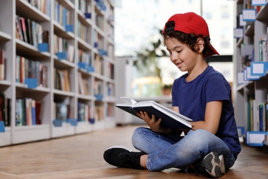 Cute little boy reading book on floor in library
