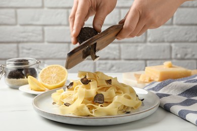 Woman slicing truffle over delicious pasta at white table, closeup