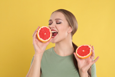 Emotional young woman with cut grapefruit on yellow background. Vitamin rich food