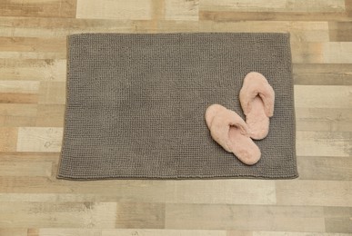 New grey bath mat with fluffy slippers on floor, top view