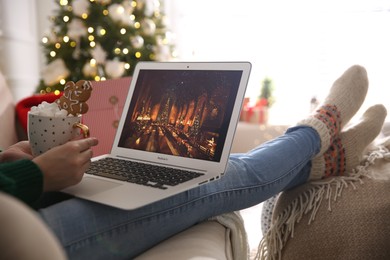 Photo of MYKOLAIV, UKRAINE - DECEMBER 25, 2020: Woman with sweet drink watching Harry Potter and Philosopher's stone movie on laptop at home, closeup. Cozy winter holidays atmosphere