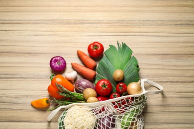 Photo of Fresh vegetables in eco mesh bag on wooden table, flat lay