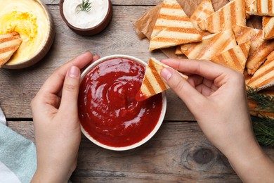 Woman dipping pita chip into sauce at wooden table, top view