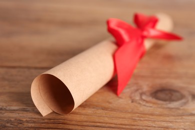Rolled student's diploma with red ribbon on wooden table, closeup