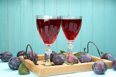 Delicious plum liquor and ripe fruits on table against light blue background. Homemade strong alcoholic beverage