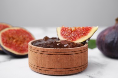 Photo of Bowl of tasty sweet fig jam and fruits on white marble table, closeup