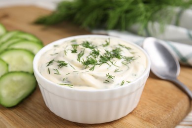 Tasty creamy dill sauce in bowl on wooden board, closeup