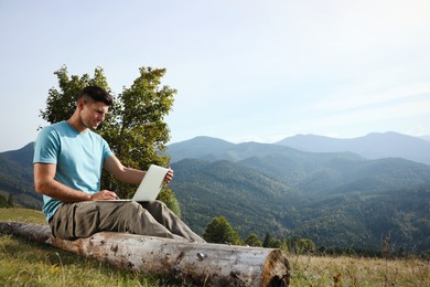 Man working with laptop in mountains on sunny day