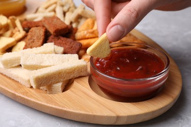Woman dipping crispy rusk in sauce at light table, closeup
