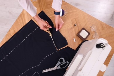 Photo of Dressmaker cutting fabric by following chalked sewing pattern in workshop, top view