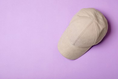 Stylish beige baseball cap on violet background, top view. Space for text