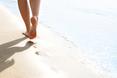 Woman walking on sandy seashore, closeup of legs