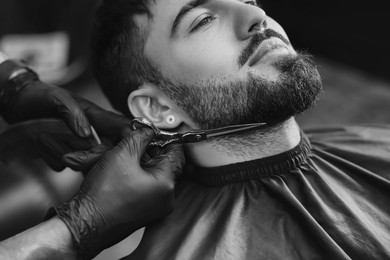 Image of Professional hairdresser working with bearded client in barbershop, closeup. Black and white effect