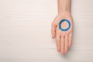 Woman showing blue circle as World Diabetes Day symbol at white wooden table, top view with space for text
