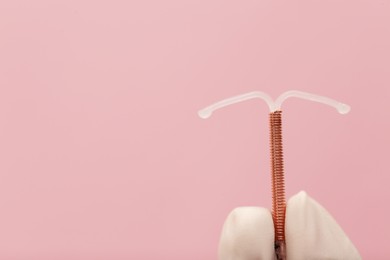Doctor holding T-shaped intrauterine birth control device on pink background, closeup. Space for text