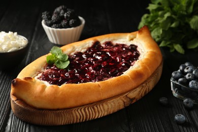 Photo of Delicious sweet cottage cheese pastry with cherry jam on black wooden table, closeup