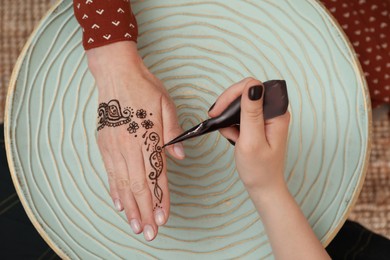 Professional mehndi master making henna tattoo at table, top view