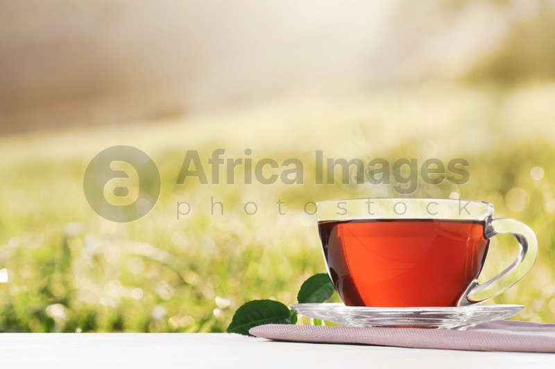 Glass cup of fresh hot tea on wooden table against blurred field. Space for text