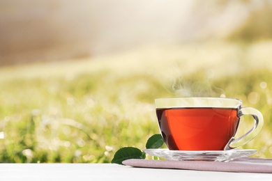 Glass cup of fresh hot tea on wooden table against blurred field. Space for text