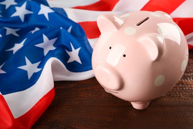 Piggy bank and American flag on wooden table, closeup