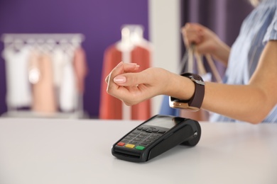 Photo of Woman using terminal for contactless payment with smart watch in shop, closeup