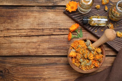 Dry calendula flowers and bottles with tincture on wooden table, flat lay. Space for text