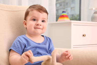 Cute baby boy with toy sitting in armchair at home
