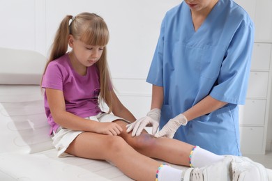 Doctor examining little girl's bruised knee in hospital