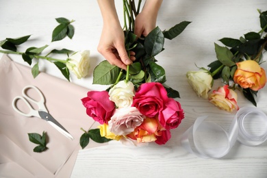 Woman making luxury bouquet of fresh roses at white wooden table, top view