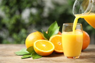 Photo of Pouring orange juice into glass at wooden table. Space for text