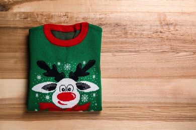 Photo of Folded warm Christmas sweater on wooden table, top view. Space for text
