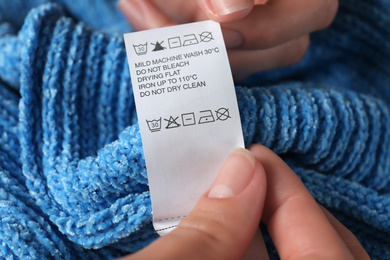 Woman reading clothing label with care symbols on blue knitted sweater, closeup
