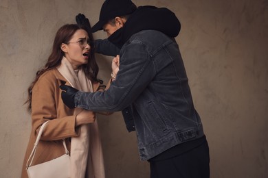 Criminal attacking young woman near beige wall. Self defense concept