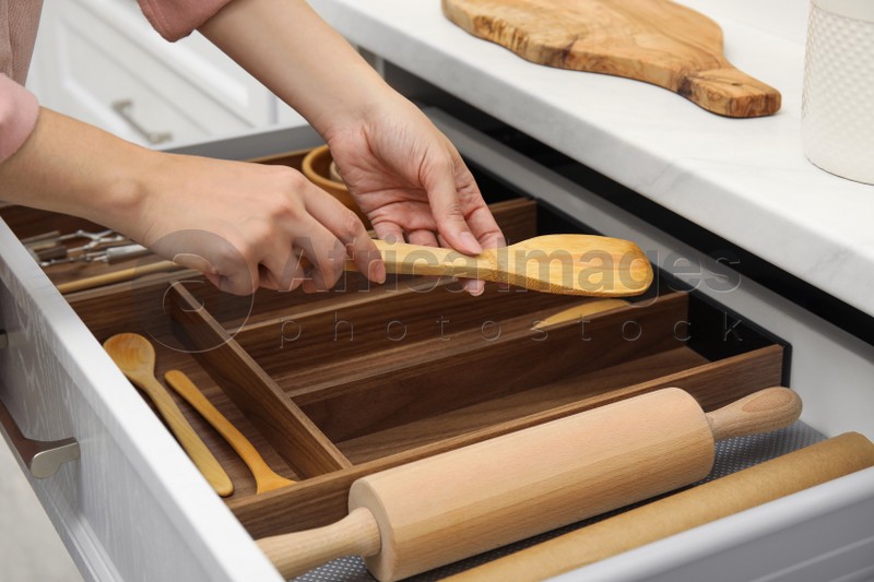 Photo of Woman putting wooden spatula into open drawer of kitchen cabinet, closeup