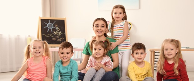 Image of Kindergarten teacher with group of children in playroom. Banner design