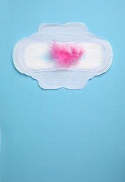 Menstrual pad with pink feather on light blue background, top view. Space for text