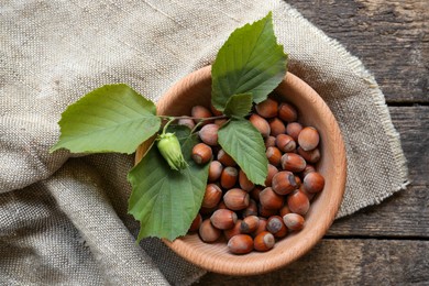 Photo of Tasty hazelnuts and green leaves on wooden table, top view. Healthy snack