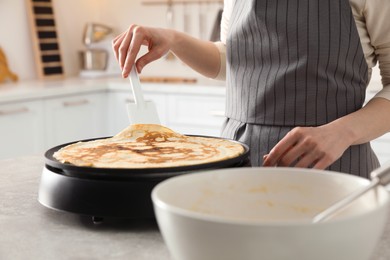 Woman cooking delicious crepe on electric pancake maker in kitchen, closeup