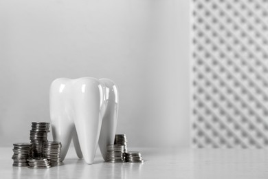 Ceramic model of tooth and coins on white table, space for text. Expensive treatment