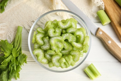 Cut fresh green celery in bowl on white wooden table, flat lay