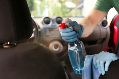 Man cleaning car salon with disinfectant spray and cloth, closeup