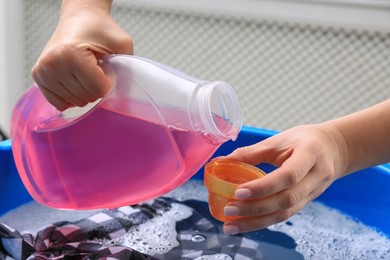 Woman pouring detergent into cap over basin with clothing, closeup. Hand washing laundry
