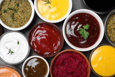 Many different sauces and herbs on black table, flat lay