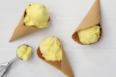 Yellow ice cream in wafer cones and scoop on white wooden table, flat lay